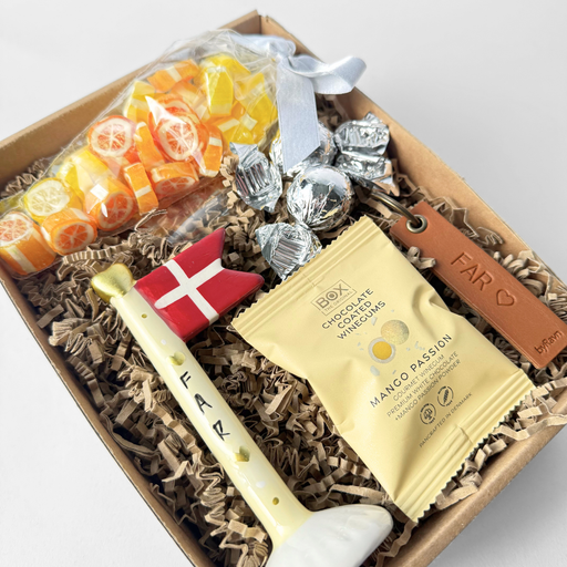 Gave til fars dag med dekorativt keramikflag, nøglering med teksten “Far” og søde sager pakket i gaveæske.